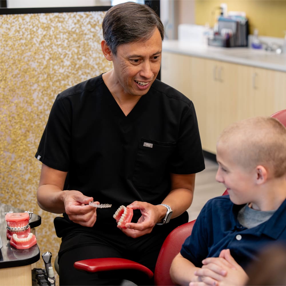 Dr. Sabelis shows a young patient a model of braces and an Invisalign tray.