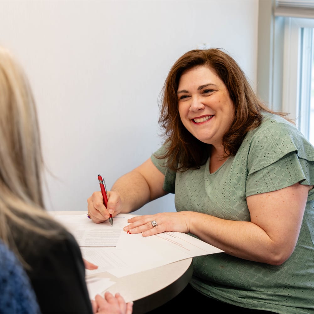 An adult patient is smiling and signing documents.