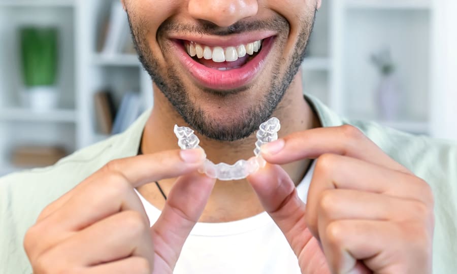 A man holds a pair of Invisalign clear aligners near his mouth.