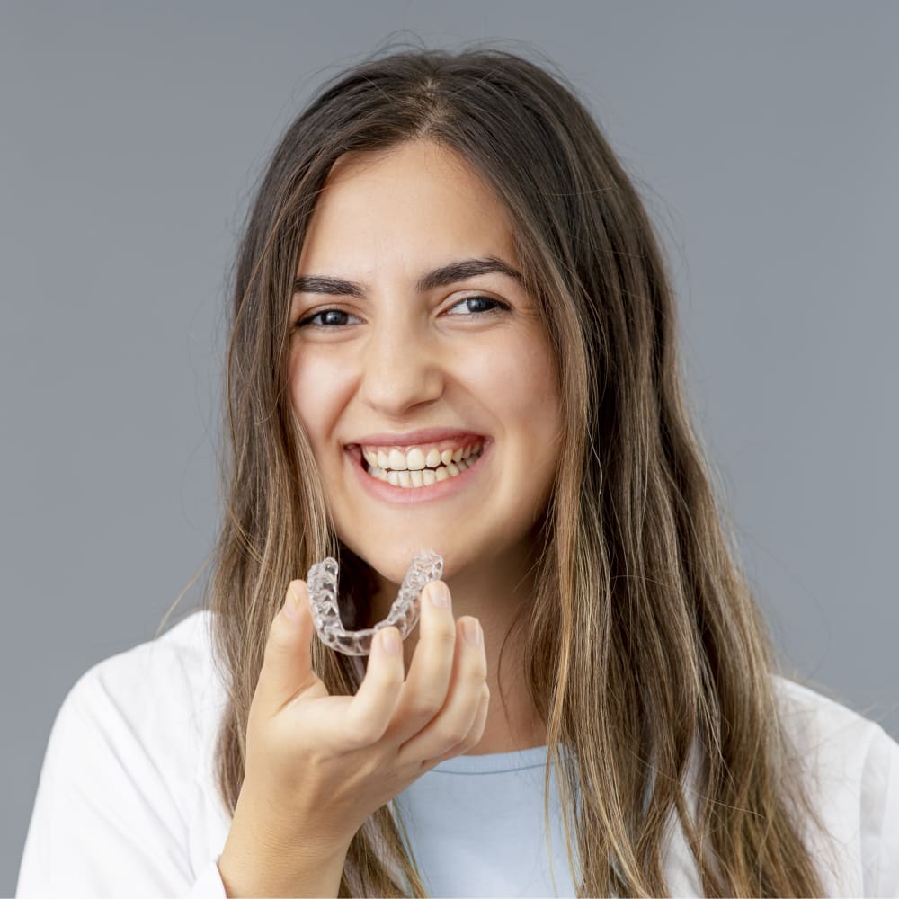 A young woman is smiling and holding an Invisalign tray up to her mouth.